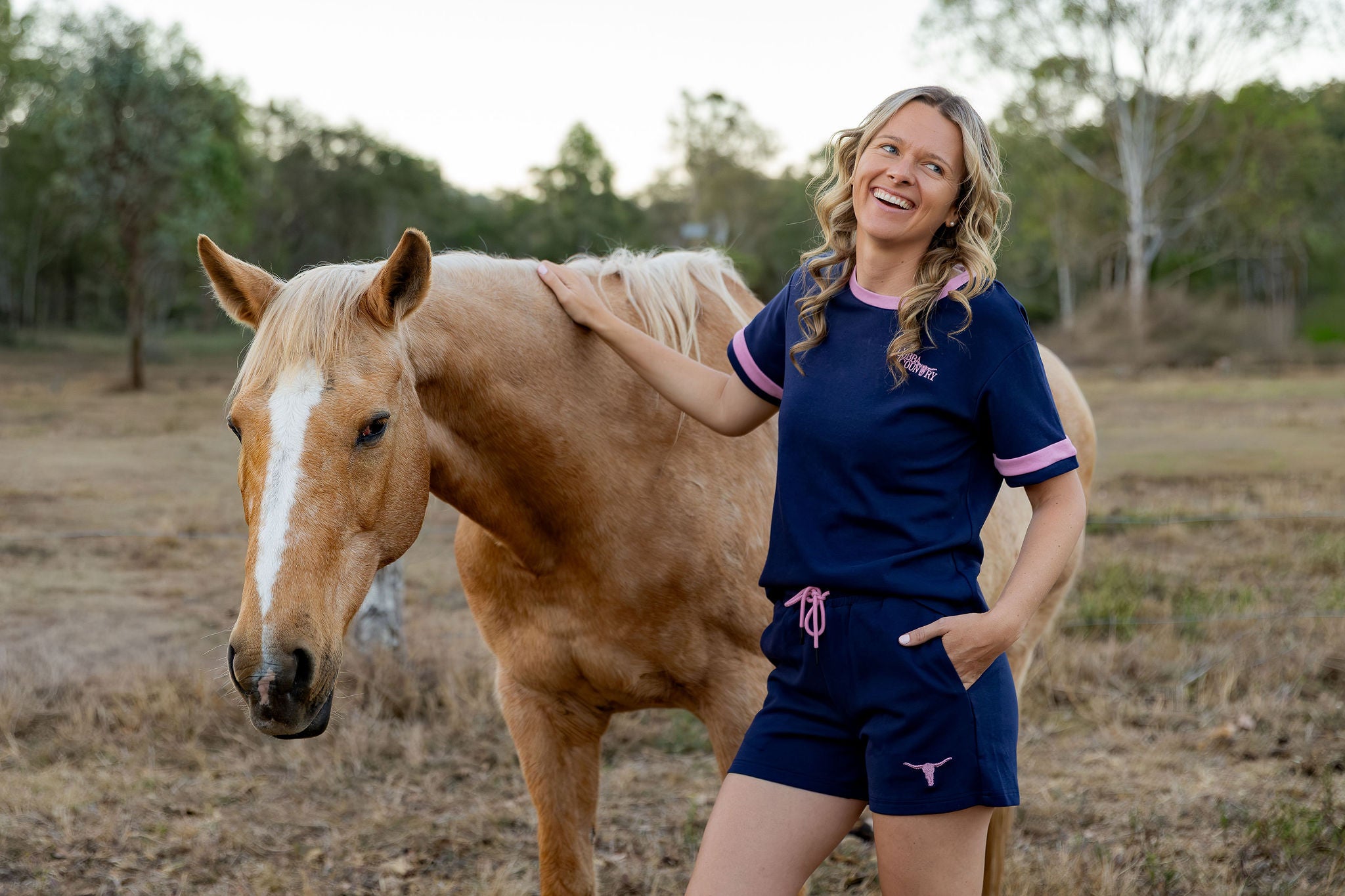 Womens navy and pink loungewear tee with embroidered Cobba Country logo and pink trim, worn with matching navy shorts beside a palomino horse