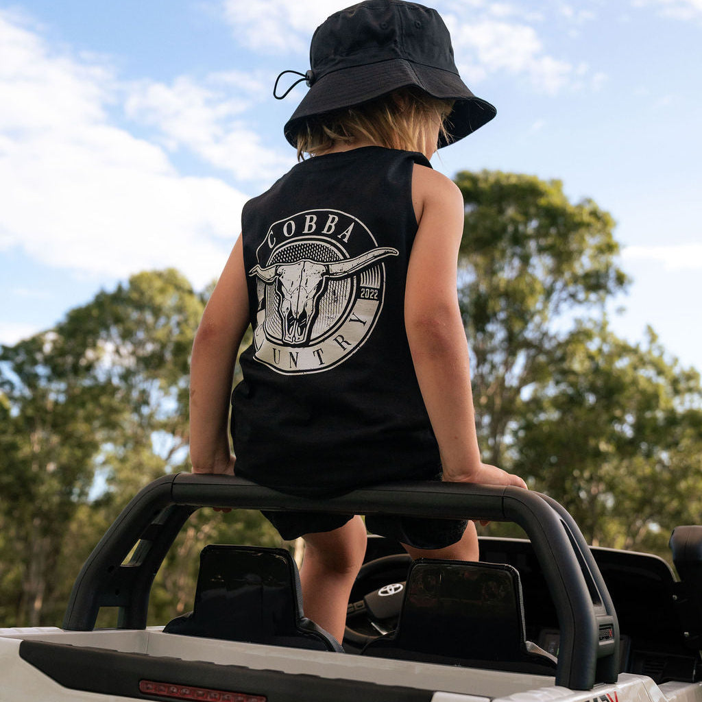Child wearing a black sleeveless shirt with a logo, sitting on the back of a Toyota Hilux Rugged X truck.