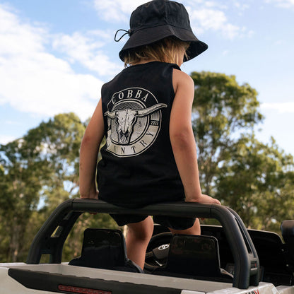 Child wearing a black sleeveless shirt with a logo, sitting on the back of a Toyota Hilux Rugged X truck.
